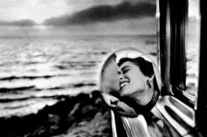 Couple sitting together and kissing, as viewed through a mirror with water in the background.